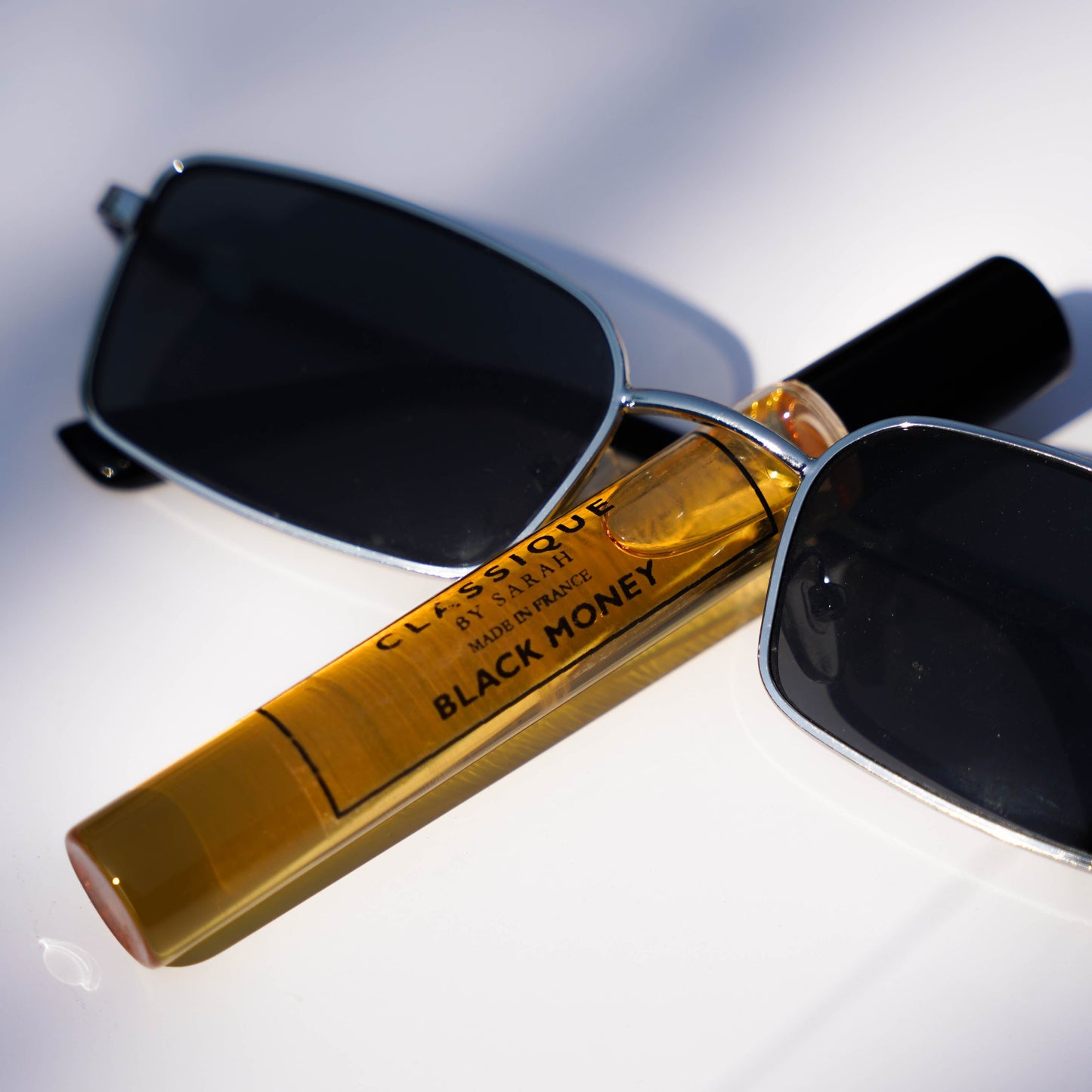 A bottle of Black Money perfume resting on a pair of sunglasses, with the bottle cap removed, against a blurred background.