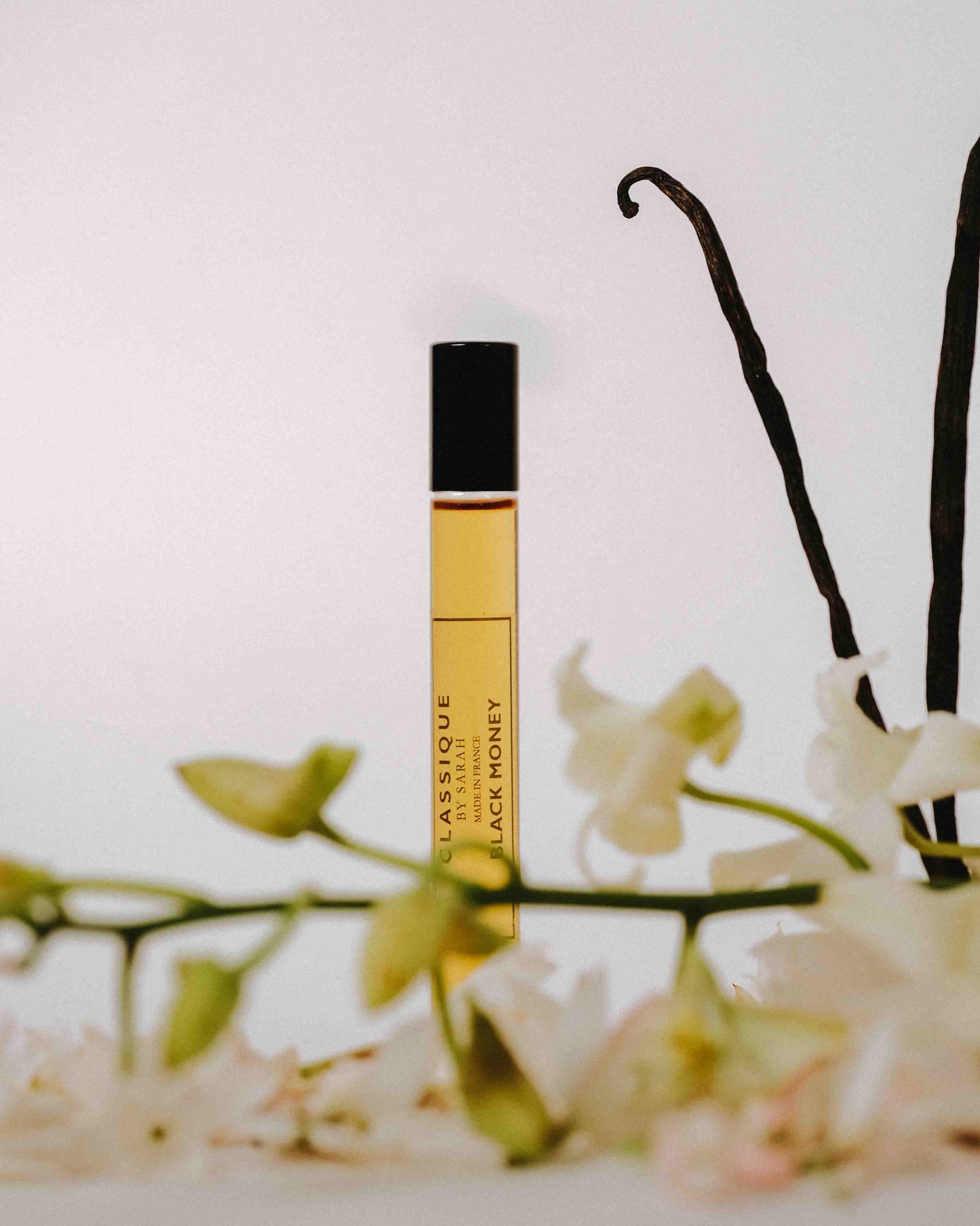 Perfume bottle labeled 'Classique' with vanilla beans and flowers on a light background