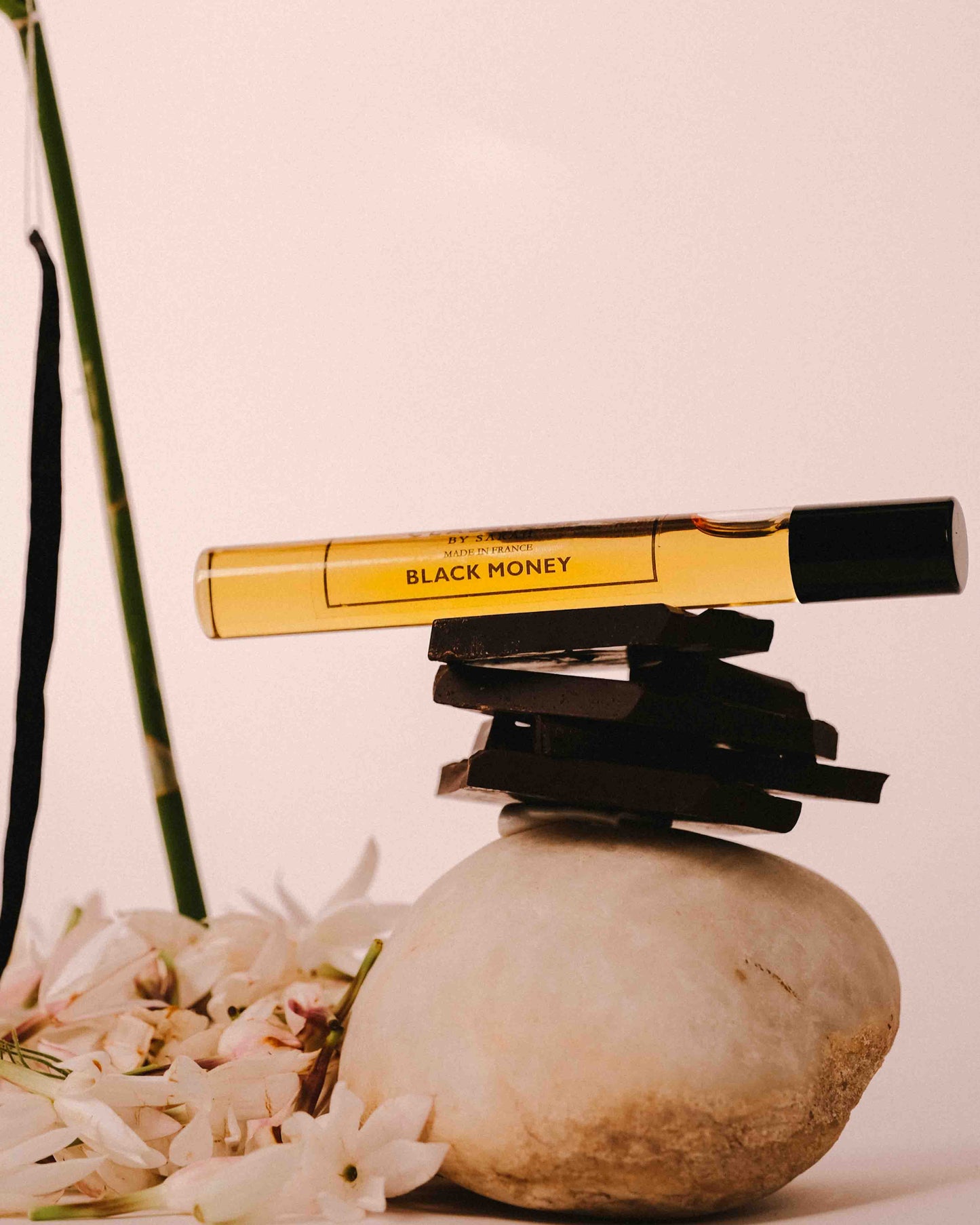 Perfume product labeled 'Black Money' on a rock with jasmine and orchid in the background