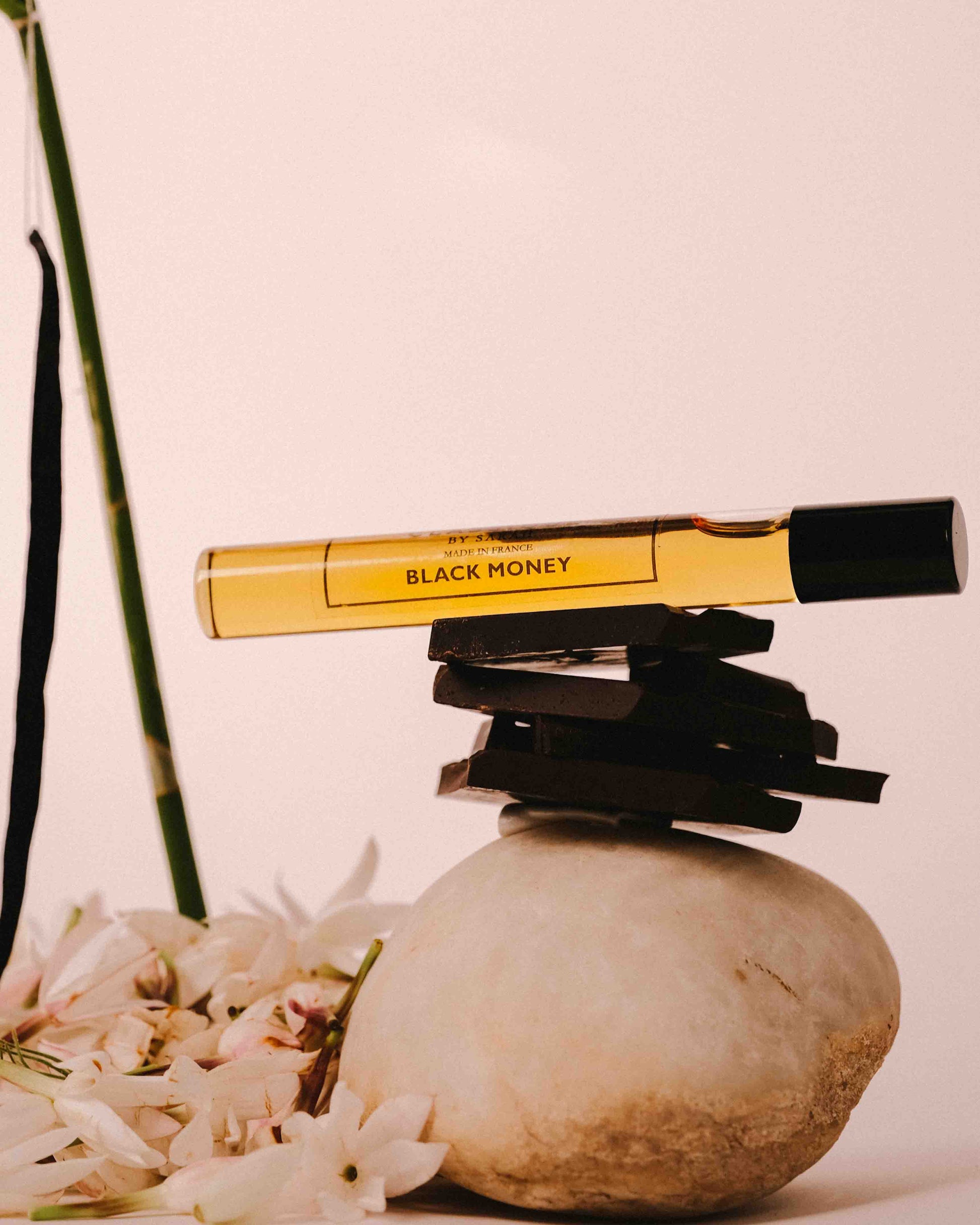 Perfume product labeled 'Black Money' on a rock with jasmine and orchid in the background